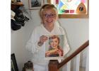 Corinne Jovaag Bustad standing by the colored glass window and the stairs leading up to her bedroom when she was a young girl. When she lived there it was all hardwood floors. The picture she is holding was from a magazine where she was featured on the front cover.